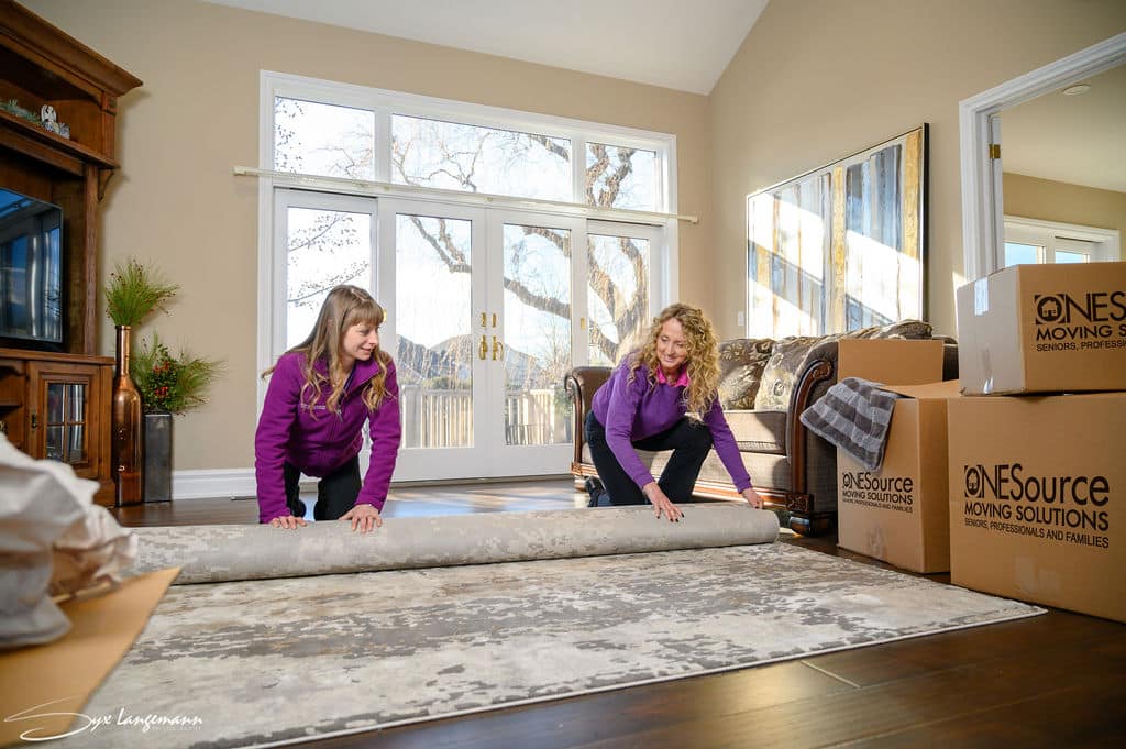 two ONESource Moving Solution team members unrolling a rug